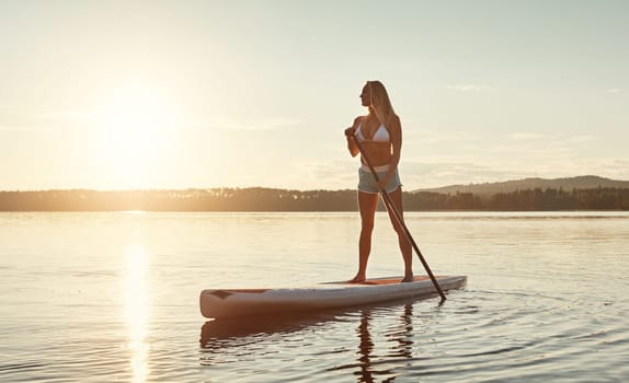 The calming beauty of nature. an attractive young woman paddle boarding on a lake.