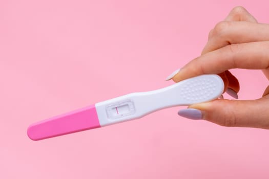 Womans hand holding negative pregnancy test with one stripe on pink background with copy space