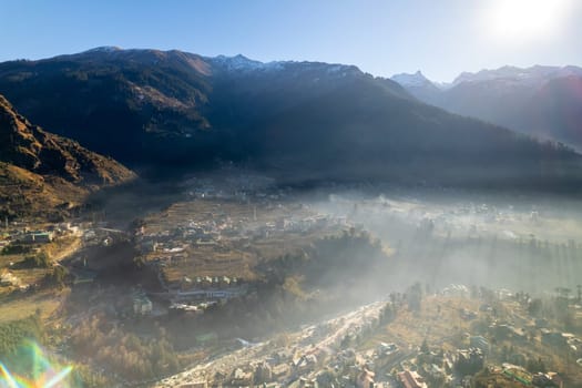 aerial drone shot gaining height over fog covered valley town of manali hill station with himalaya range in distance showing this popular tourist destination