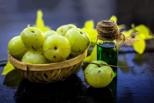 Close-up of Indian gooseberry with its extracted essence or concentration in a transparent bottle on a wooden surface with raw amla in a fruit and vegetable basket.