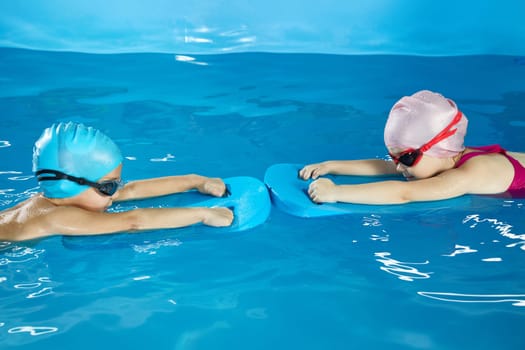Little girl and boy learning to swim in indoor pool with pool board