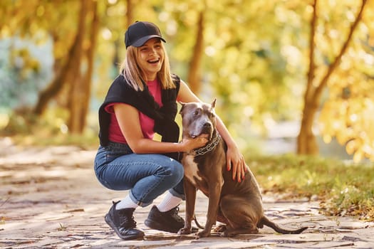 Having fun. Woman in casual clothes is with pit bull outdoors