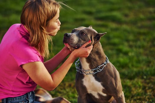 Outdoors on the field. Woman in casual clothes is with pit bull