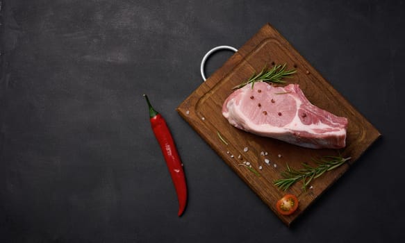 Raw pork tenderloin on the bone and spices on a wooden cutting board. Portion for lunch and dinner, top view. Copy space