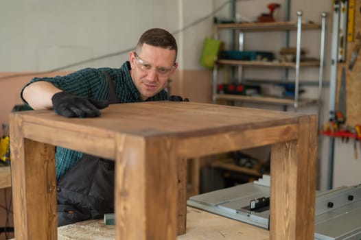 Male carpenter finishing work on wooden table in workshop.