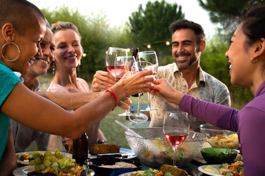 Diverse happy friends toasting with wine and beer during garden dinner party. Friends having fun.