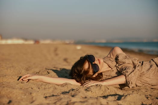 woman in a dress and sunglasses relaxing on the beach in windy weather. High quality photo