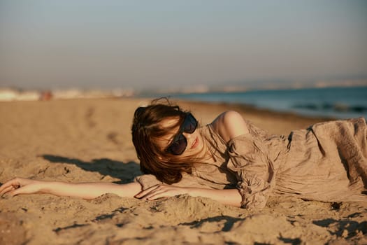 a woman in black sunglasses lies on the sand with her arms outstretched