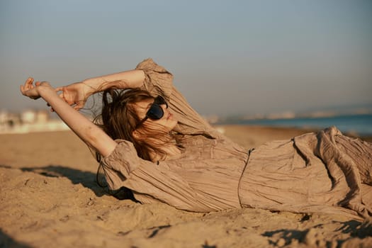 a woman in black sunglasses lies on the sand with her arms outstretched