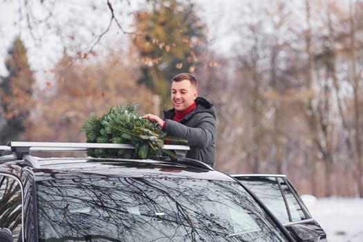 In the forest. Man with little green fir is outdoors near his car. Conception of holidays