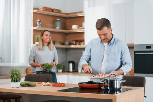 Helping each other. Couple preparing food at home on the modern kitchen