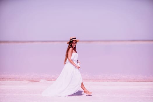 Woman in pink salt lake. She walks in a white long dress and hat along the salty white shore of the lake. Wanderlust photo for memory