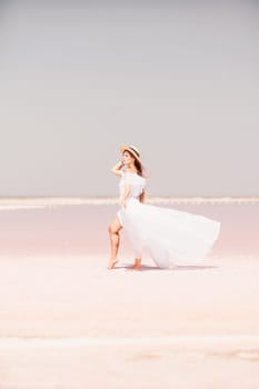 Woman in pink salt lake. She walks in a white long dress and hat along the salty white shore of the lake. Wanderlust photo for memory