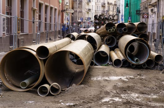 Pipelines of different diameters lie behind a fence on a city street.