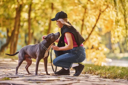 Having a walk. Woman in casual clothes is with pit bull outdoors