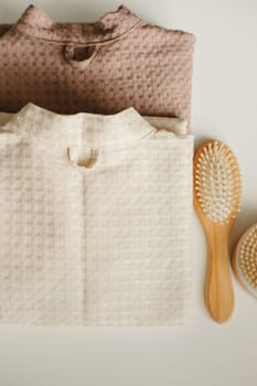 On a white surface are two bathrobes, a comb and a washcloth