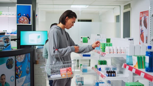 Male customer analyzing supplements boxes on pharmacy shelves