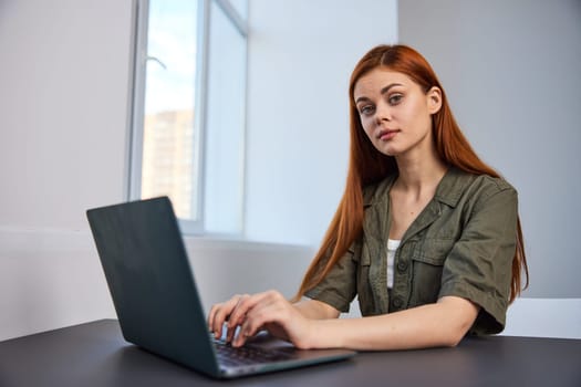 pensive redhead woman sitting at laptop while working in office