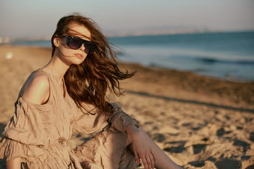 portrait of a woman in dark sunglasses sitting in a dress on the seashore