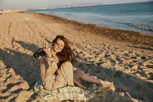 a woman in dark sunglasses sits near the sea on a blanket in windy weather. High quality photo