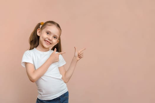 Cute smiling caucasian preschool girl in a white t-shirt points to an empty space