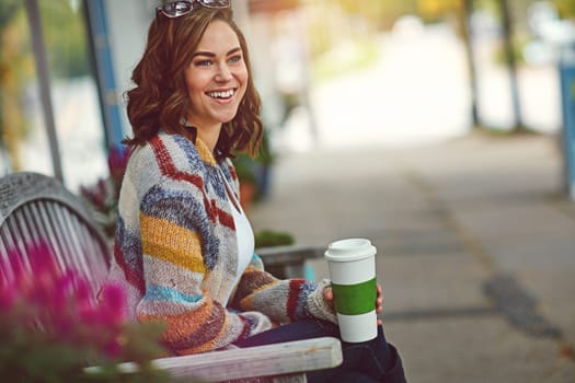 Starting the weekend with a caffeine kick. a happy young woman drinking coffee while relaxing on a bench downtown.