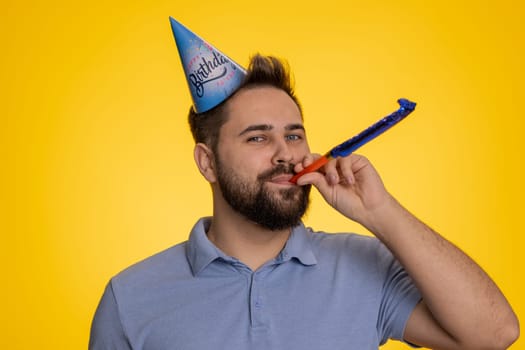 Happy excited lucky man wearing birthday hat cone blow pipe celebrating party success win victory