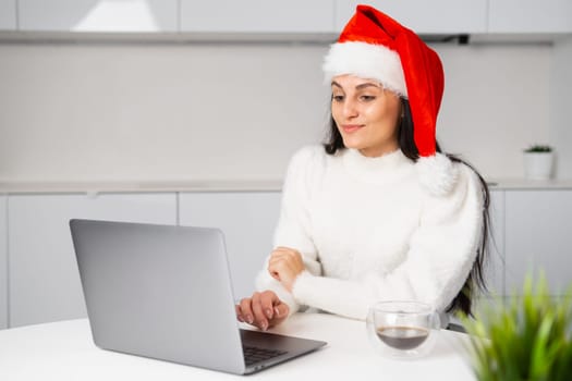 Cute Santa Claus woman working at home using a notebook. Freelancer works on Christmas holidays.