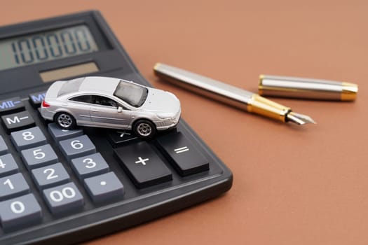Toy car, calculator and pen on a brown background. Car rental, purchase or insurance.