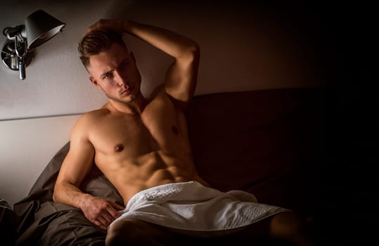 Shirtless sexy male model lying alone on his bed
