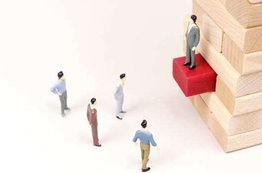 On a white surface, a leader stands on wooden blocks, figures of people are below.