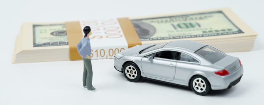 On a white surface is a car, a pack of dollars and a miniature figure of a man.