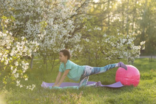 a little girl does yoga lying on a sports mat in the park. a healthy lifestyle is a childish habit