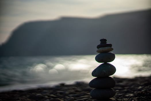 Pebble pyramid silhouette on the beach. Sunset with sea in the background. Zen stones on the sea beach concept, tranquility, balance. Selective focus