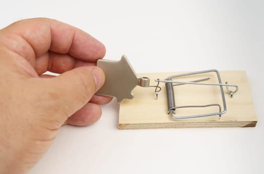 A man's hand is trying to pull a metal figurine of a house out of a mousetrap.