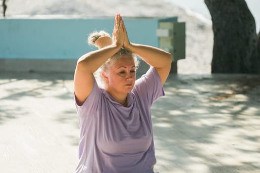Mature elderly woman with dreadlocks doing pose during yoga training in park on summer day. Healthy active senior female practicing asana on mat in morning on fresh air