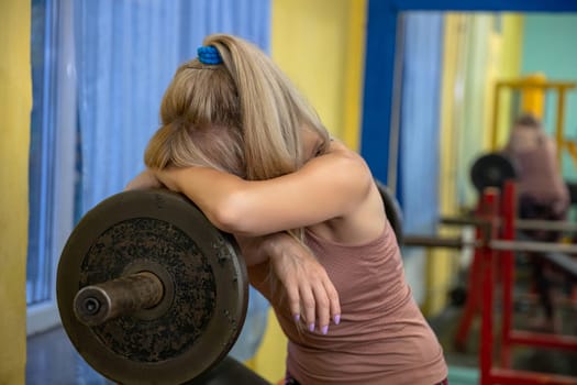Woman leans against exercise barbell burying her head in her hands