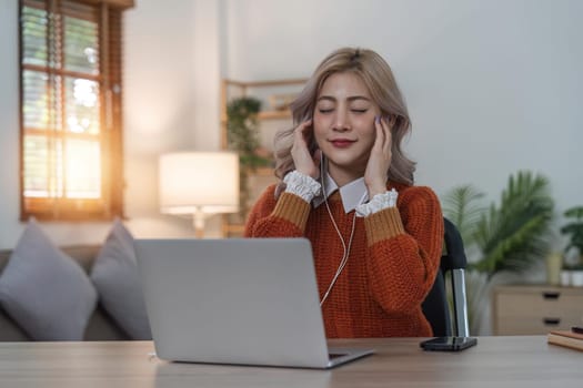 Relaxed woman listening to music with headphones pass laptop at home