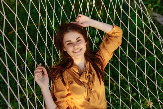 a close horizontal photo from above of a happy, pleasantly smiling woman lying on a mesh hammock in nature on a sunny day