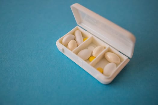 different capsules lie in a white open pill box on a blue background. View from above