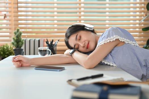 Pretty young asian woman wearing headphone fall asleep distracted from work, sleeping at working desk