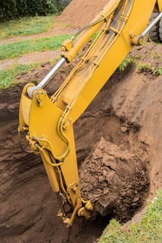 The hydraulic piston of the excavator bucket with the ground digs a hole on the construction site close-up