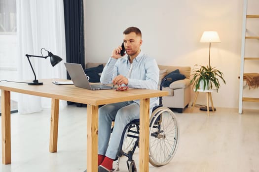 Using laptop. Disabled man in wheelchair is at home