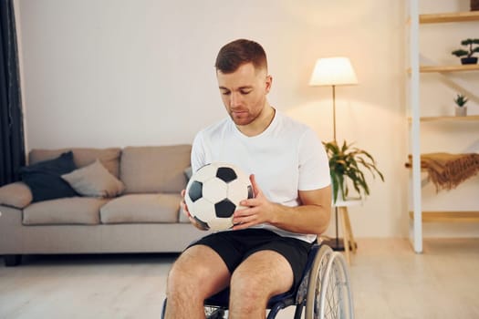With soccer ball. Disabled man in wheelchair is at home