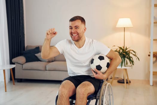 Soccer fan with ball. Disabled man in wheelchair is at home