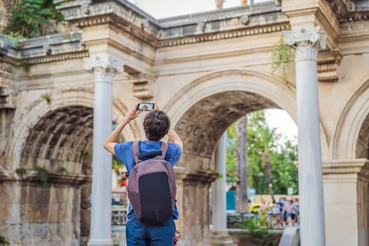 Happy male tourist traveler discover interesting places and popular attractions and walks in the old city of Antalya. Hadrian Kapisi turkey landmark city history. Popular tourist attraction - ancient Roman Hadrian Gate in old town Antalya, Turkey on a summer day. Turkiye