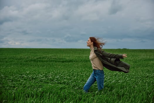 a woman in a coat stands in a field in cloudy weather resisting a strong wind. High quality photo