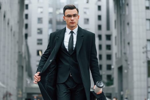 Walking forward. Businessman in black suit and tie is outdoors in the city