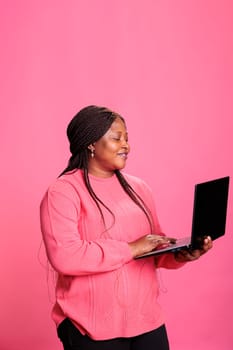 Smiling cheerful woman with pink t-shirt holding laptop computer studying for univerisity