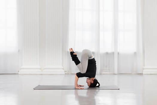 Side view of an athletic woman doing headstand training during yoga meditation in a bright gym. Concept of normalization of all processes in the body, strength, energy and concentration